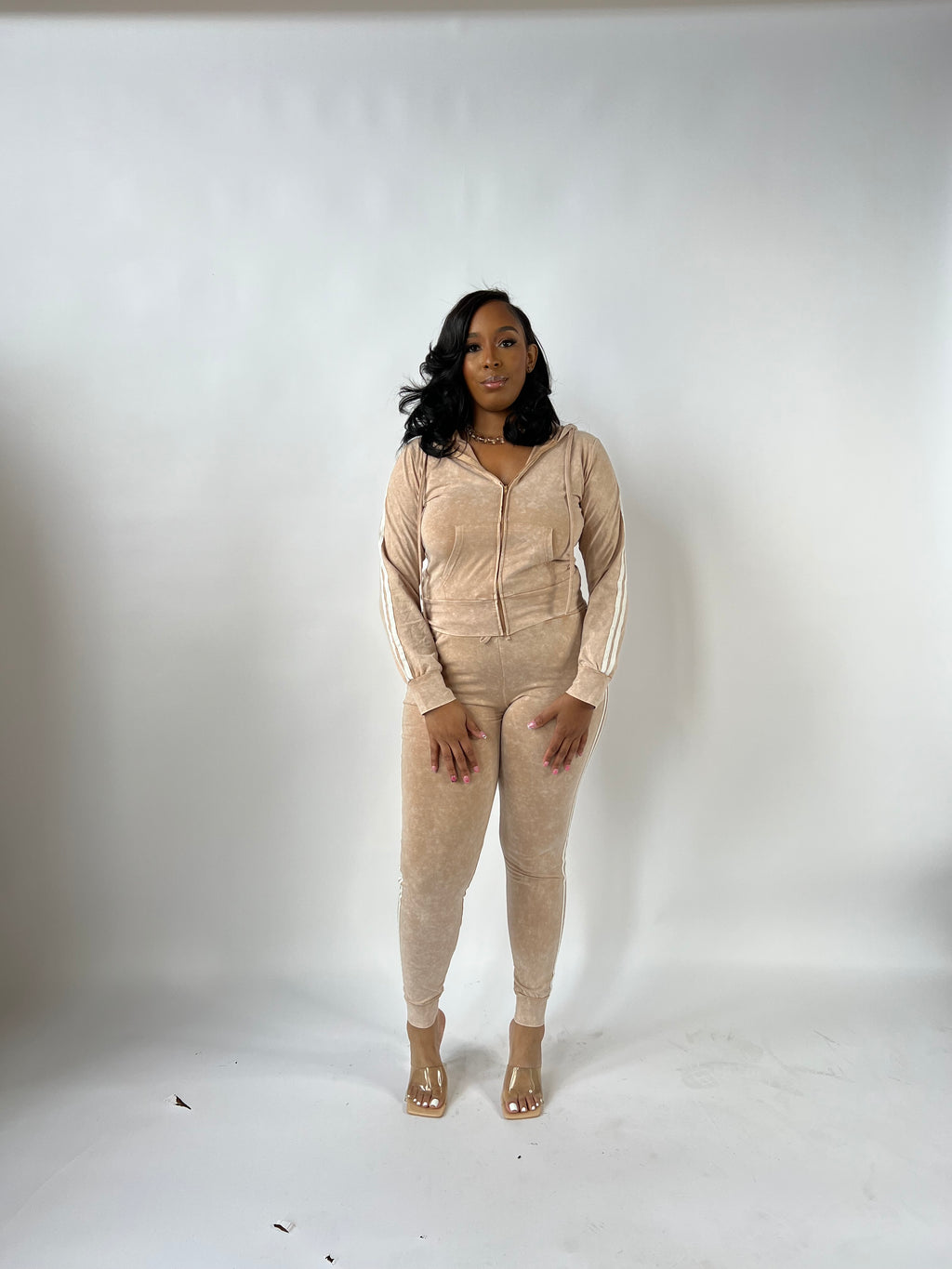 A model wearing a mocha brown 2-piece track set with a zip-up hoodie and high-waisted pants with white stripes on the side.