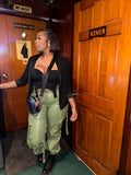 A person wearing green faux leather cargo pants with a black top,  the pants include cargo like pockets, latches, and accessorized placements for a good finish.