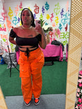 A person wearing orange high-waisted cargo pants, gold accented buttons, denim like cloth.