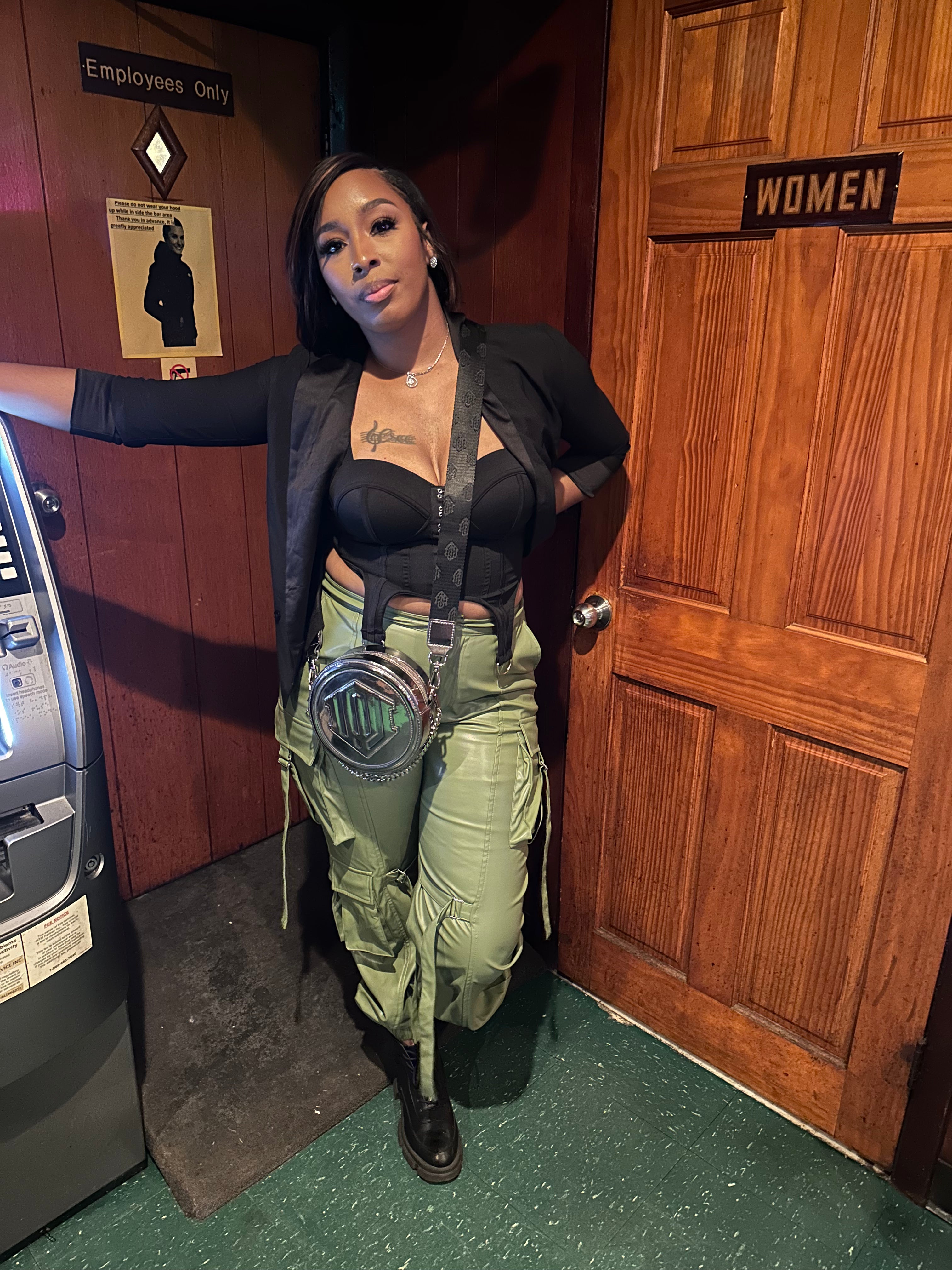 A person wearing green faux leather cargo pants with a black top,  the pants include cargo like pockets, latches, and accessorized placements for a good finish.