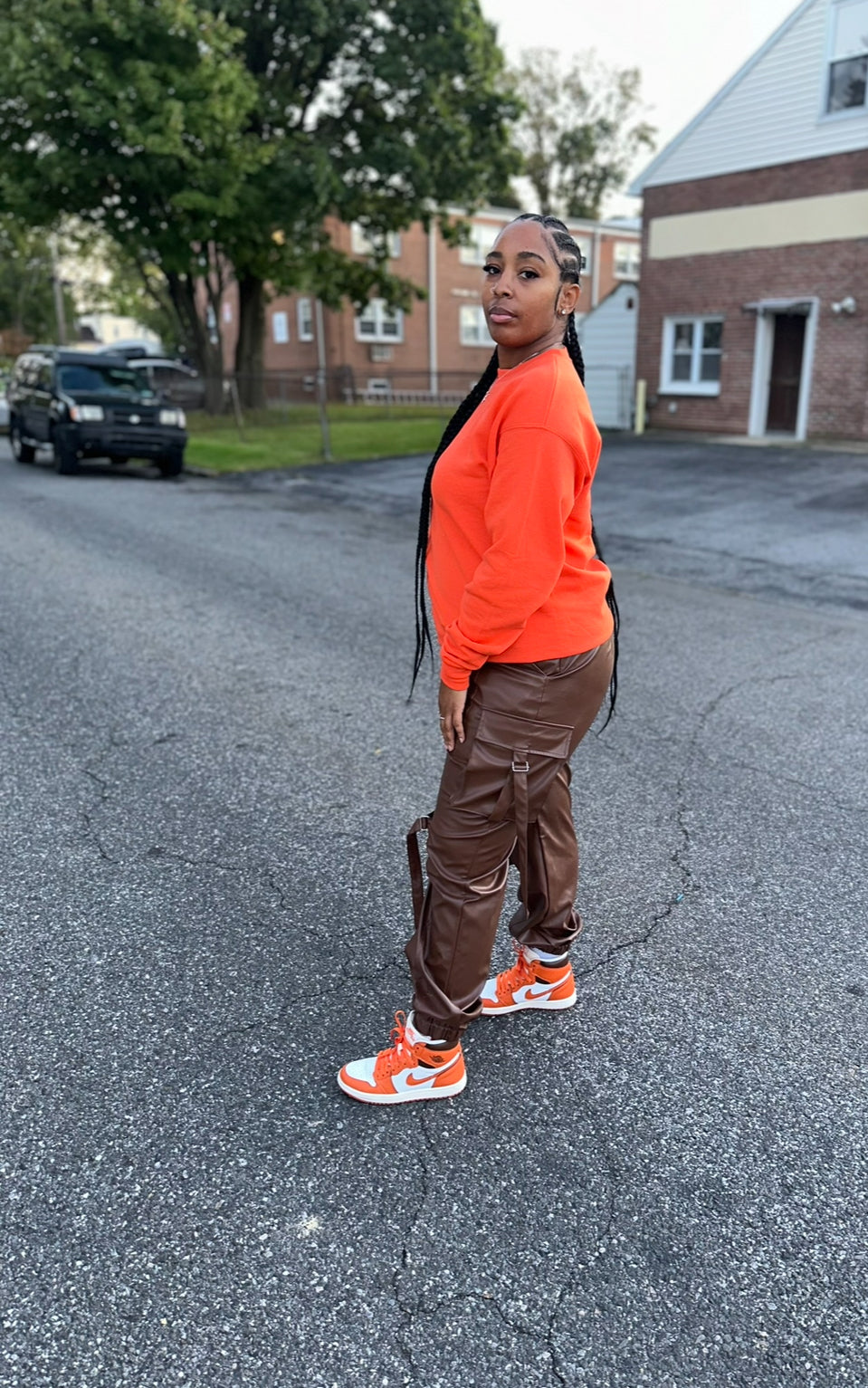 A person wearing chocolate brown cargo pants with an orange top,  the pants include cargo like pockets, latches, and accessorized placements for a good finish.