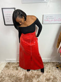 A person wearing a red, solid-colored skirt that reaches until the ankles, paired with a black top and black pants. The image shows the person from the shoulders up, looking to the side.