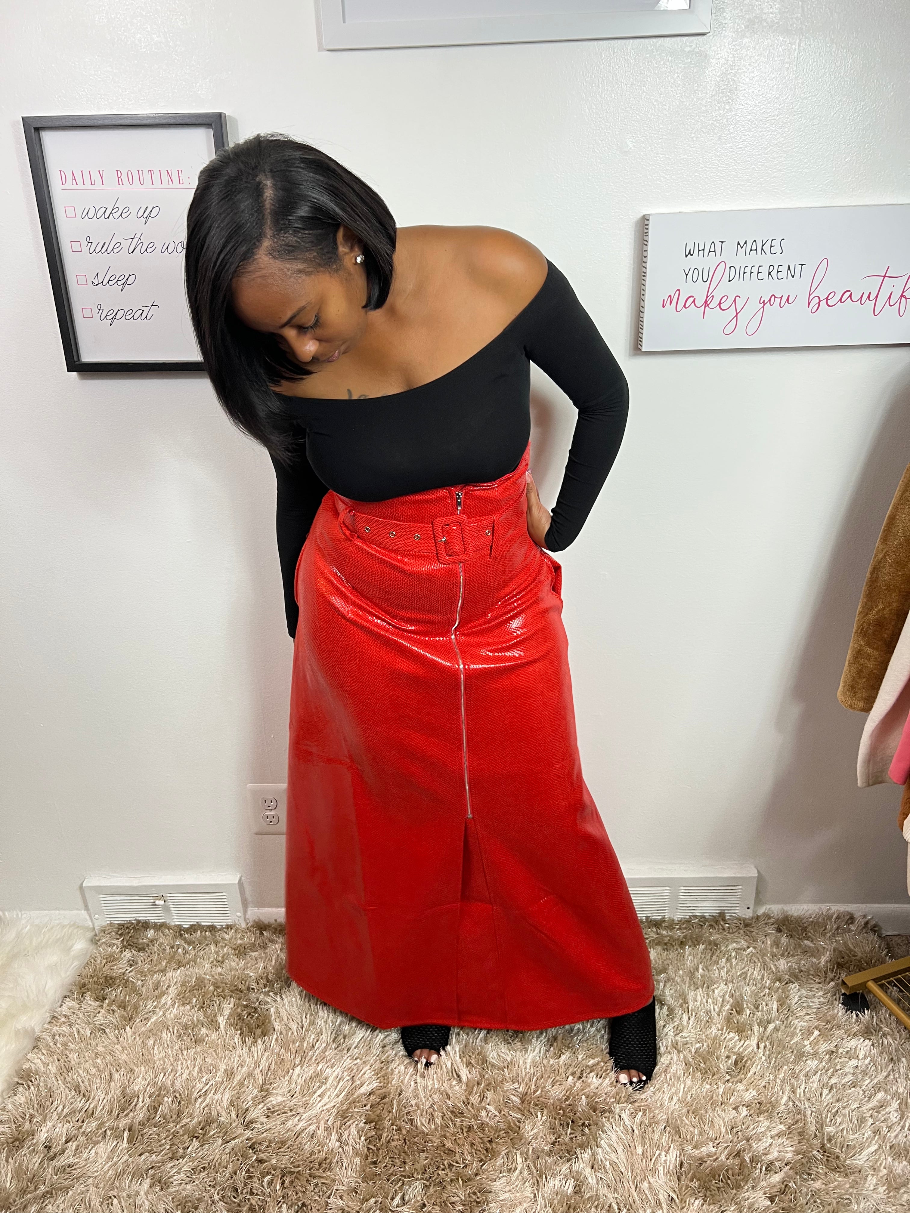 A person wearing a red, solid-colored skirt that reaches until the ankles, paired with a black top and black pants. The image shows the person from the shoulders up, looking to the side.